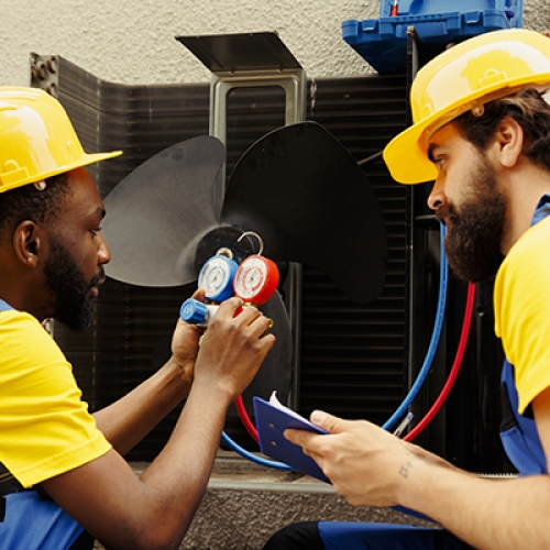 Meticulous wiremen expertly refilling freon in external air conditioner while using manifold measurement device to closely measure the pressure in HVAC system, ensuring perfect cooling performance